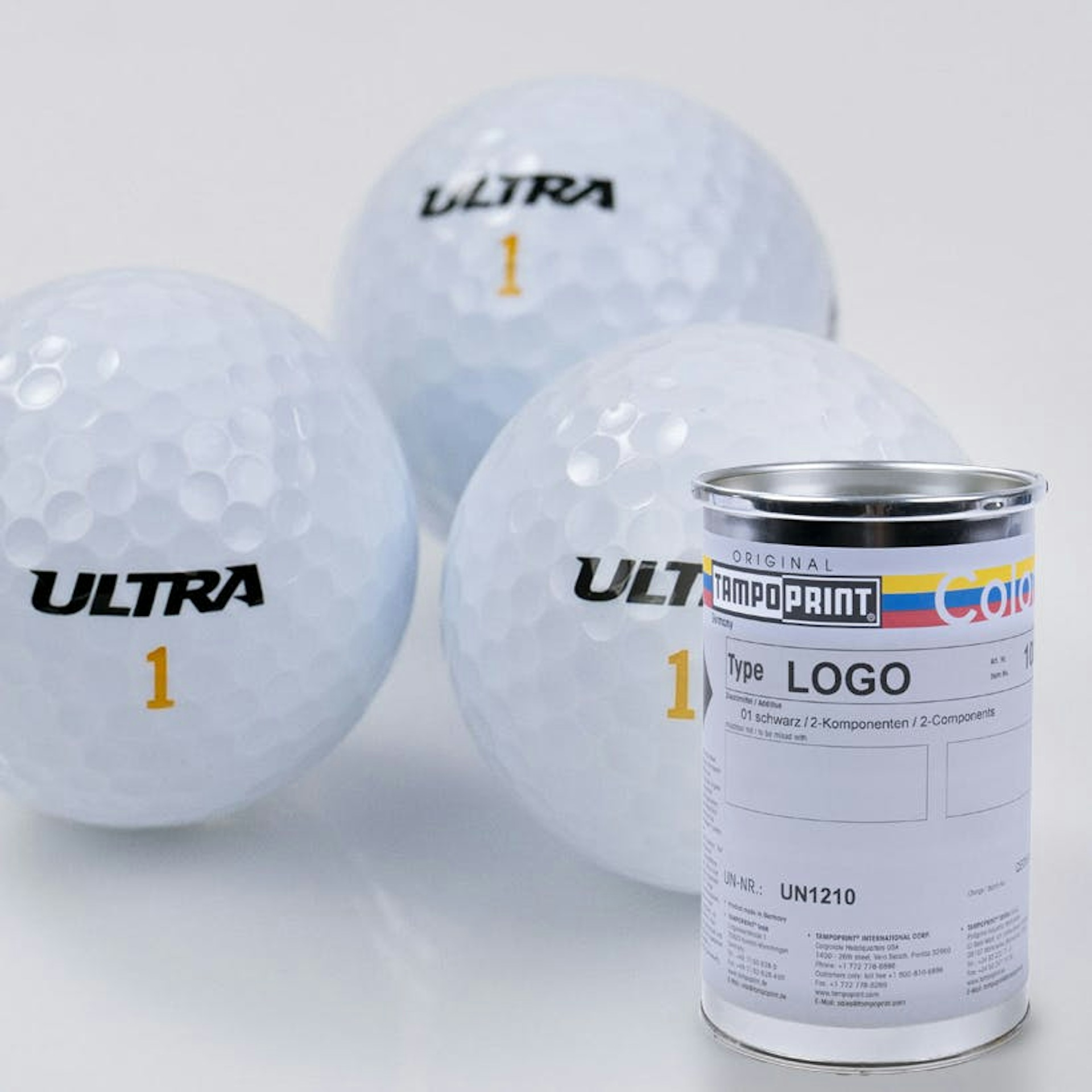 Eine Type LOGO Tampondruckfarbdose mit bedruckten Golfbällen im Hintergrund. 