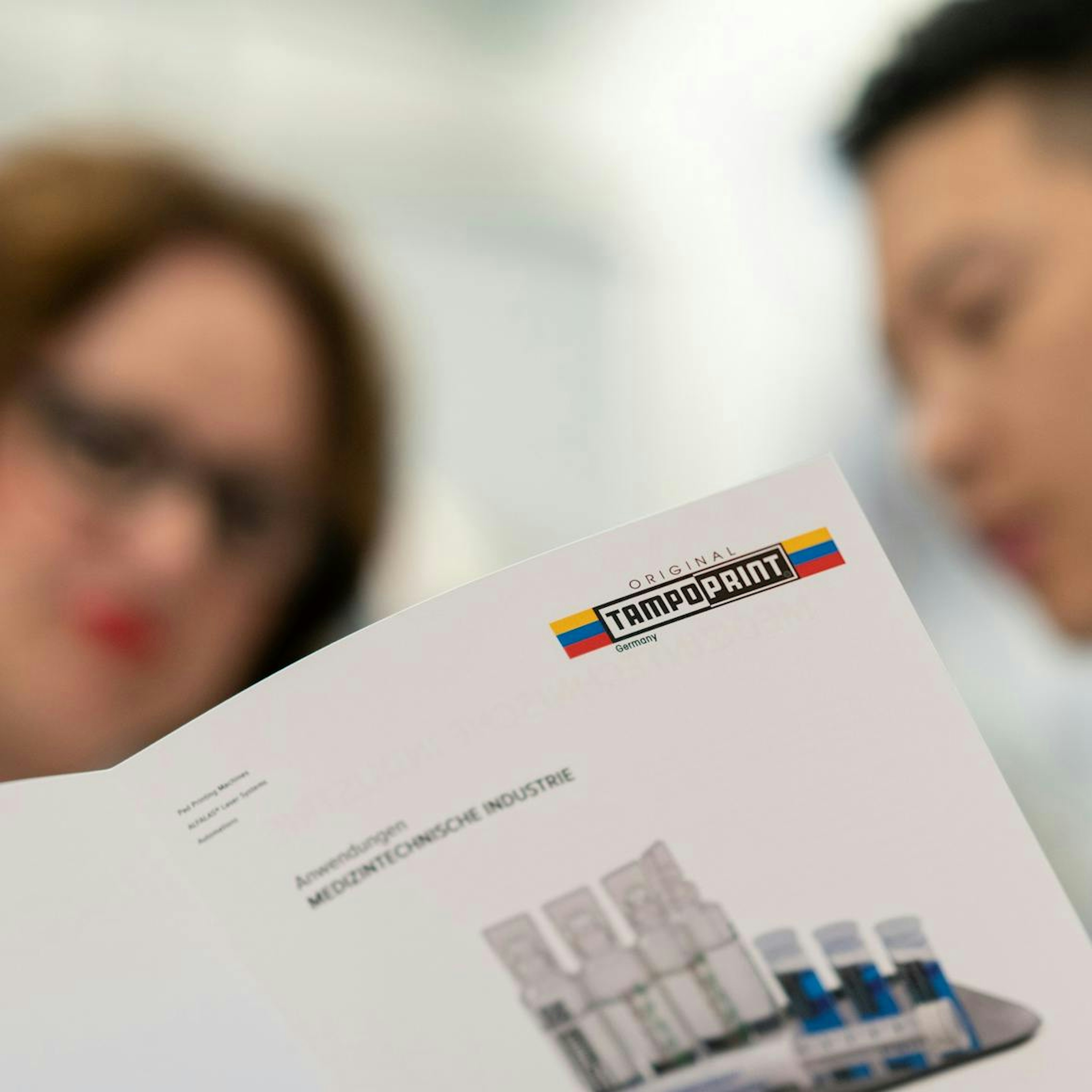 Zwei Vertriebsmitarbeiter schauen gemeinsam in eine Broschüre für Tampondruckanwendungszwecke im medizintechnischen Anwendungsbereich.  